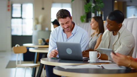 Two-Businessmen-Working-On-Laptop-In-Informal-Seating-Area-Of-Modern-Office-On-Coffee-Break