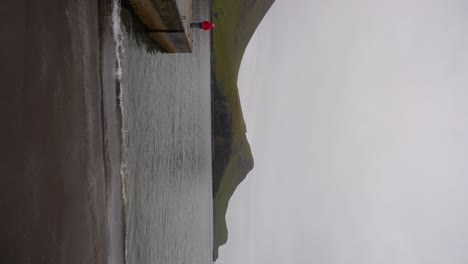 Woman-pondering-Faroese-landscape,-looking-at-Atlantic-Ocean-from-Bour-pier-in-Vagar