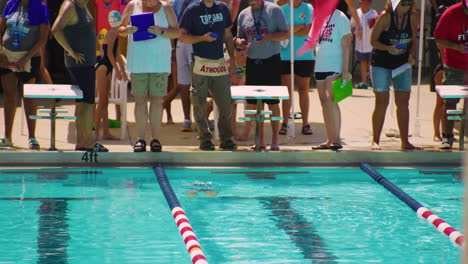 Slowmo-telephoto-shot-of-swimmer-athlete-arriving-last-at-race,-judges-on-sides