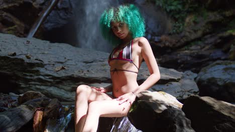 Junges-Bikinimädchen-Mit-Grünen-Haaren-Sitzt-Am-Fuße-Eines-Wasserfalls-In-Der-Karibik