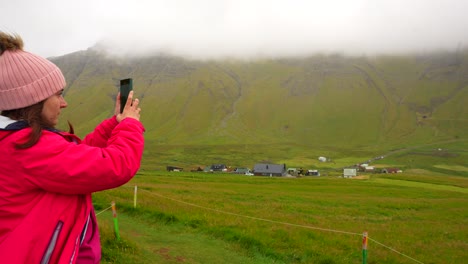 Female-tourist-filming-Faroese-landscape-with-phone-camera-in-Gasadalur-village,-Faroe-Islands