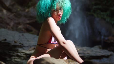 Green-hair-bikini-girl-sits-at-the-base-of-a-flowing-waterfall-in-the-Caribbean