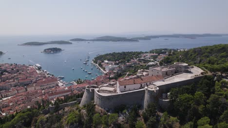 Magnificent-view-across-medieval-castle-onto-Hvar-harbor,-aerial-orbit