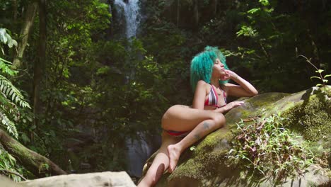 A-woman-laying-on-a-rock-in-a-bikini-with-a-flowing-waterfall-in-the-background