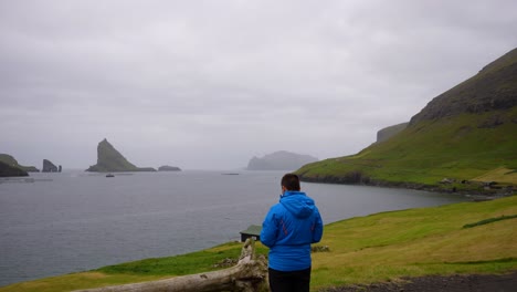 Man-flying-drone-by-Atlantic-Ocean-in-Faroe-Islands-with-view-of-Drangarnir-sea-stacks-and-Tindholmur-in-fog