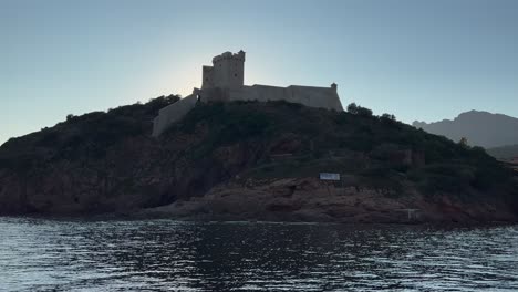 Girolata-castle-and-harbour-at-sunset-seen-from-sailing-boat-touring-Corsica-island-in-France