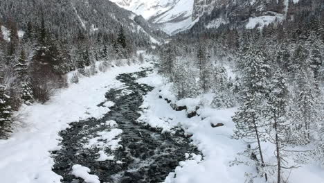 Drone-follows-the-course-of-a-river-in-a-snowy-mountainous-environment-in-the-Swiss-Alps