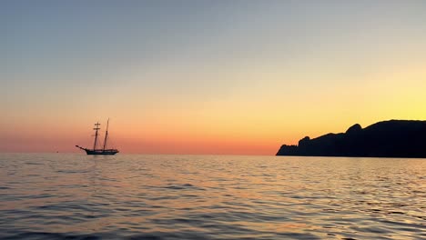 Backlight-view-of-ancient-sailing-ship-with-lowered-sails-navigating-at-sunset-or-sunrise-seen-from-moving-boat