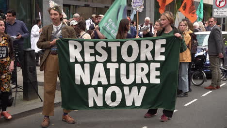 Two-people-hold-a-green-banner-that-reads,-“Restore-Nature-Now”-on-a-protest-outside-the-The-Department-for-Environment-Food-and-Rural-Affairs-