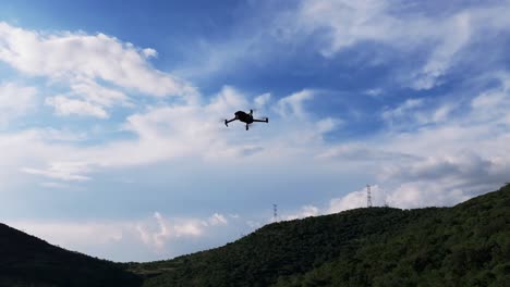Orbit-around-silhouette-of-quad-copter-drone-flying-against-cloudy-sky-and-mountainous-region-background