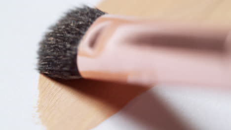 Brushing-a-layer-of-make-up-foundation-on-a-clean,-white-palette-board-to-check-its-texture-and-tone