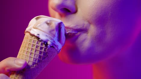 Close-up-of-a-young-pretty-woman-eating-a-vegan-ice-cream-with-vegan-chocolate-and-enjoying-the-delicious-taste-in-front-of-purple-background-in-slow-motion