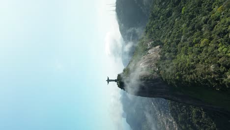 Vertical-drone-shot-showing-famous-Christ-The-Redeemer-Statue-on-green-hilltop-of-Rio-De-Janeiro---orbiting-shot