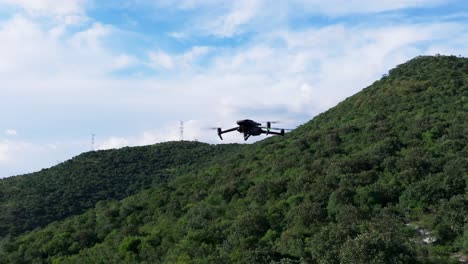 Orbit-around-drone-quadcopter-silhouette-hovering-against-tropical-lush-green-mountain-backdrop
