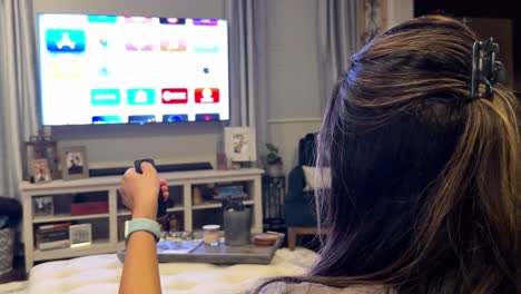 Rear-view-of-woman-scrolling-streaming-apps-on-TV,-using-remote-control,-at-home