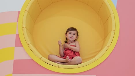 Happy-laughing-toddler-eating-Lollipop-candy-sitting-inside-circular-wall-built-in-sofa