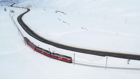 Aerial-drone-shots-featuring-a-vibrant-red-train-gliding-through-a-snow-covered-wonderland