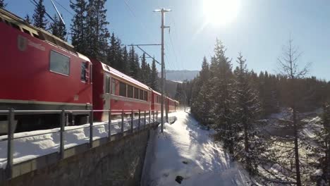 Aerial-drone-shots-featuring-a-vibrant-red-train-gliding-through-a-snow-covered-wonderland
