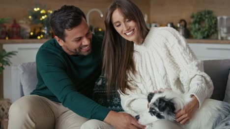 Glückliches-Paar-Mit-Mehreren-Ethnien,-Das-Mit-Hund-Spielt,-Während-Es-Zu-Weihnachten-Auf-Dem-Sofa-Sitzt.