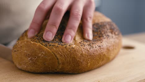 Close-up-of-hands-of-woman-cutting-fresh-bread--at-the-kitchen.