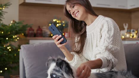 Woman-chilling-with-dog-on-sofa-with-mobile-phone-during-the-Christmas.