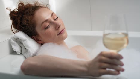 Caucasian-redhead-woman-taking-a-bath-and-drinking-wine.