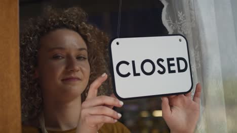 Caucasian-waitress-changing-sign-on-doors-from-closed-to-open.