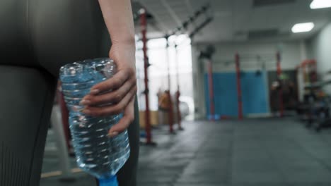 Young-woman-having-walking-through-the-gym-while-holding-a-bottle-of-water.