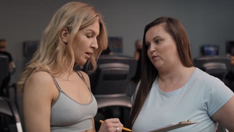 Woman-with-overweight-talking-with-female-trainer-in-the-gym.
