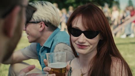 Close-up-of-caucasian-ginger-hair-woman-drinking-beer-from-disposable-cup-at-music-festival-and-chatting-with-friends.