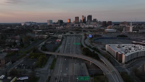 Cinematic-aerial-view-of-Downtown-Atlanta-Freeway-with-the-view-of-famous-skyline-buildings-in-the-background-at-sunset,-Traffic-on-the-highway-in-an-urban-modern-city-in-the-USA