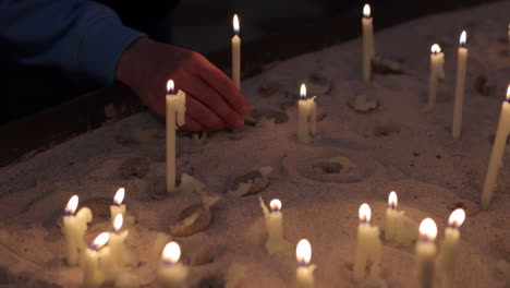 Worshiper-Place-Prayer-Candle-On-Sand-Inside-A-Church---close-up