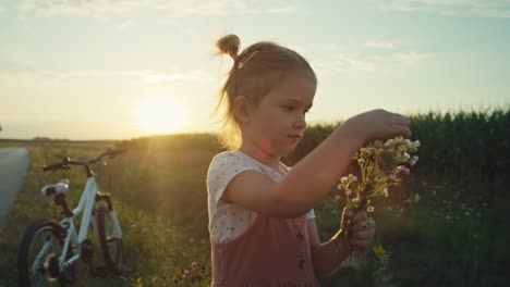 Little-caucasian-girl-spending-time-on-village-road-and-picking-wildflowers.