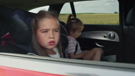 Fröhliches-Kaukasisches-Mädchen-Von-8-Jahren,-Das-Während-Einer-Autofahrt-Aus-Dem-Autofenster-Schaut,-Und-Ihre-Schwester-Im-Hintergrund.