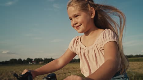 Tilt-up-of-elementary-age-caucasian-girl-riding-a-bike-bike-at-sunset-time.