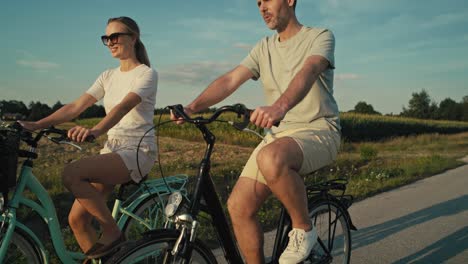 Side-view-of-playful-caucasian-couple-having-fun-while-riding-a-bike-on-sunset-on-village-road.