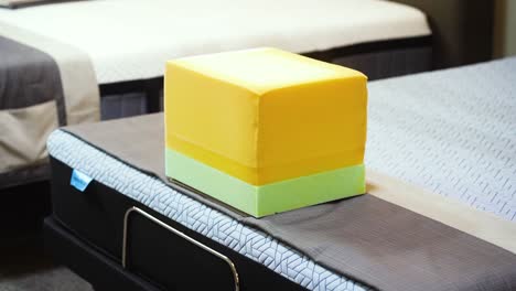 Ein-Großer-Gelb-grüner-Block-Mit-Demonstrationsmatratzenbett,-Memory-Schaumstoff-Und-Industriellem-Komfortmaterial-Liegt-Auf-Einer-Neuen-Matratze-In-Einem-Möbelgeschäft