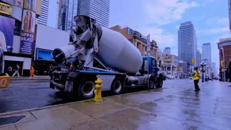 Cement-trucks-being-directed-by-Traffic-Controller-on-Young-and-Charles-in-downtown-Toronto-Southside-with-wet-streets-on-a-sunny-summer-day-reflective-pavement-clouds-clearing-after-storm-clearing-up