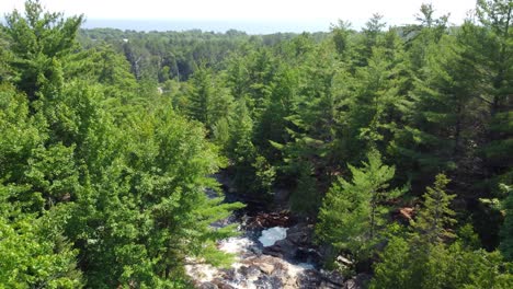 Aerial-drone-shot-following-the-fast-flowing-white-waters-of-the-Duchesnay-Falls,-as-the-river-cascades-down-over-the-rocks-and-through-a-forest,-North-Bay,-Canada