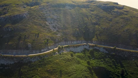 Aerial-pan-of-narrow-mountain-road-below-the-peaks-at-sunrise