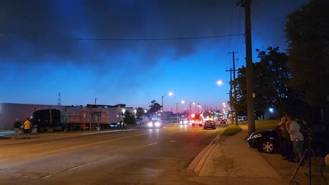 A-wide-angle-view-from-a-sidewalk-of-a-busy-road-as-a-fire-engine-arrives-responding-to-an-emergency-call-for-a-warehouse-factory-fire