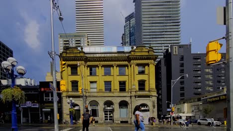 Yonge-and-Charles-downtown-Toronto-iconic-historical-bank-building-converted-into-fast-food-coffee-shop-offices-and-fitness-center-over-shadowed-by-modern-architectural-futuristic-advancements-wet-sun
