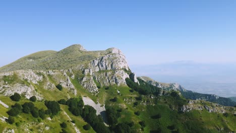 Drone-flight-around-rocky-mountain-peak-and-a-small-forest-at-high-altitude