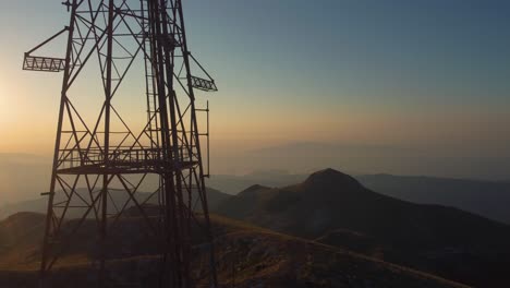 Aerial-pan-of-the-silhouette-of-a-telecommunications-tower-on-a-mountain-peak-at-sunrise
