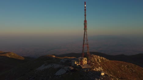 Aerial-approaching-large-telecommunications-tower-on-a-mountain-peak-at-sunrise