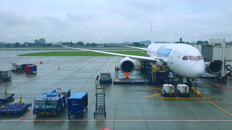 Airplane-being-carried-timelapse-by-crew-operating-container-loader-before-departure-and-takeoff-on-a-rainy-day-with-ground-support-equipment-and-crews