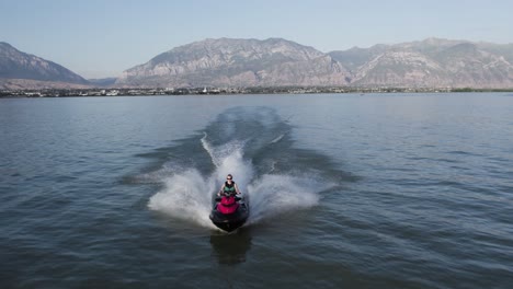Mujer-Montando-Jet-Ski-Waverunner-En-La-Superficie-Del-Lago-Utah-En-Verano,-Seguimiento-Aéreo