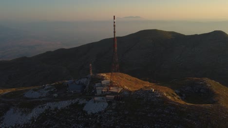 Slow-aerial-of-telecommunications-tower-on-a-mountain-peak-at-sunrise