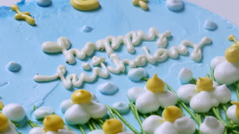 Zooming-out-of-a-blue-birthday-cake,-covered-in-blue-frosting-and-decorated-with-white,-yellow-tipped-flowers
