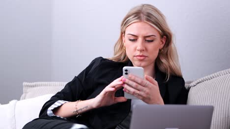 A-young-businesswoman-sits-on-the-sofa-and-surfs-on-her-cell-phone-medium-shot